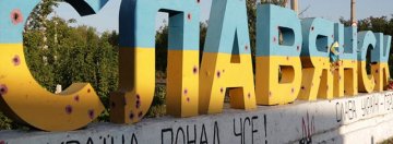 Blaszany napis "Słowiańsk" w narodowych kolorach ukraińskich, ze śladami po kulach, umieszczony na betonowym cokole, stojący przy drodze prowadzącej do miasta.