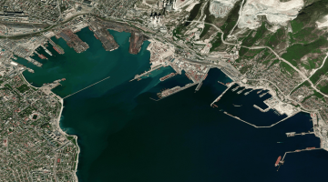 Widok satelitarny z lotu ptaka na port w Noworosyjsku – widoczne nabrzeża, doki, terminale przeładunkowe oraz przybrzeżna zabudowa miejska.