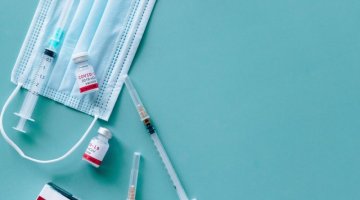 Zdjęcie pokazuje maseczkę ochronną, strzykawkę i szczepionki przeciw COVID-19